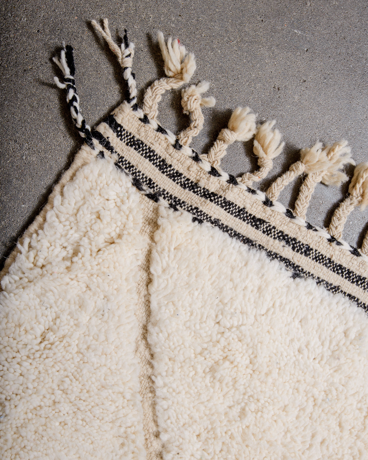 Corner of beniourain rug with tightly woven end and natural wool tassels.